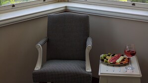 A corner with a chair and a small table with a fruit platter and a glass of red wine.