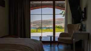 A hotel room with a bed, a chair, a small table, and a view of a landscape through a large window.