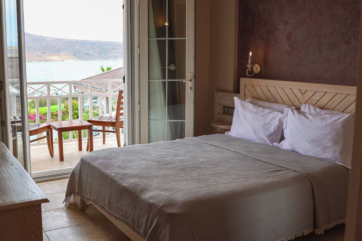 Un dormitorio con cama, mesita de noche, lámpara y vistas al exterior.
