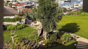A marina with boats docked, a grassy area with a tree, and a hillside in the background.