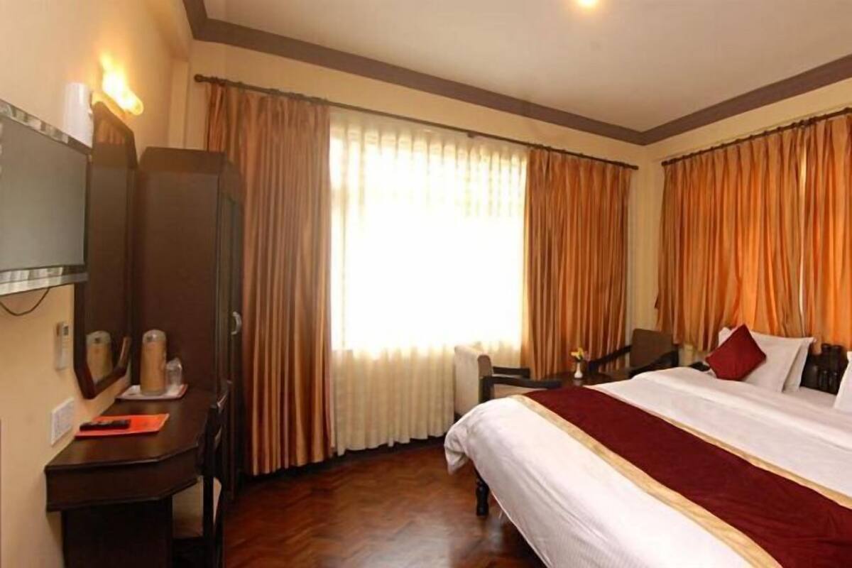 Una habitación de hotel con una cama grande, un escritorio con silla, un televisor y cortinas.