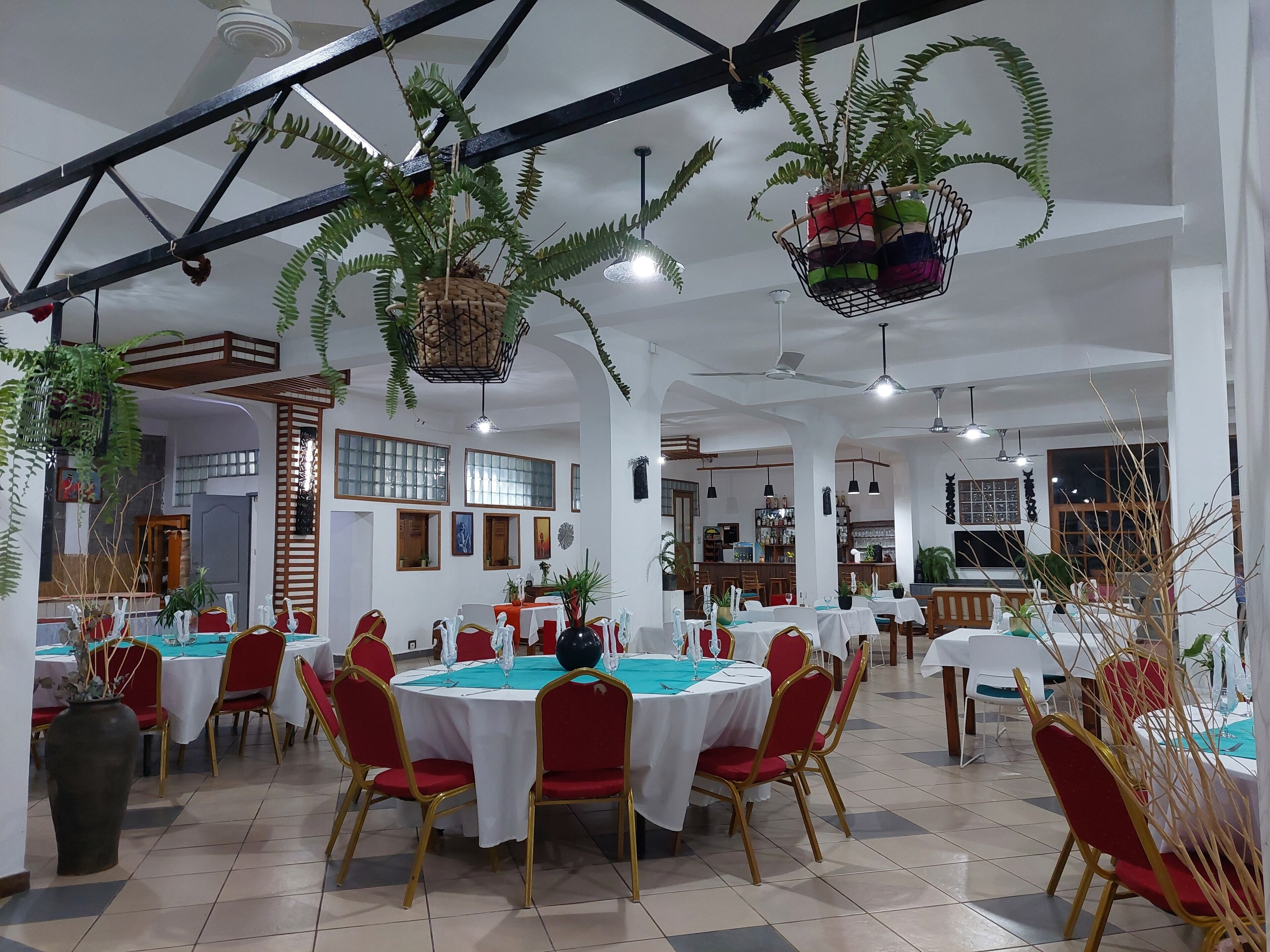Un vaste espace dédié à la salle à manger, avec des tables rondes, des chaises rouges et des plantes suspendues.