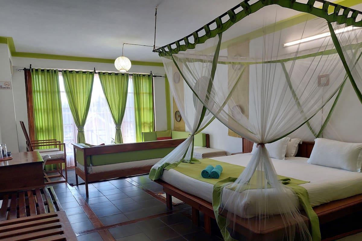 A room with a bed under a canopy, a bench, a table, and curtains.