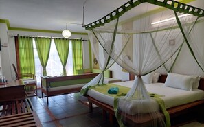 Habitació amb un llit sota una bugenvila, una banca, una taula i cortines.