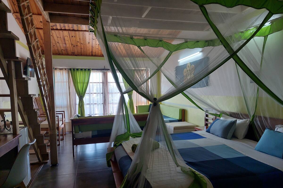A room with a bed under a mosquito net, a wooden staircase, and a window with curtains.