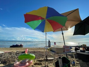 A beach scene with a colorful umbrella, a cooler, and a table with a 'Dunkin'' sign. - Experience tranquility and entertainment all in one place! (Calatagan)