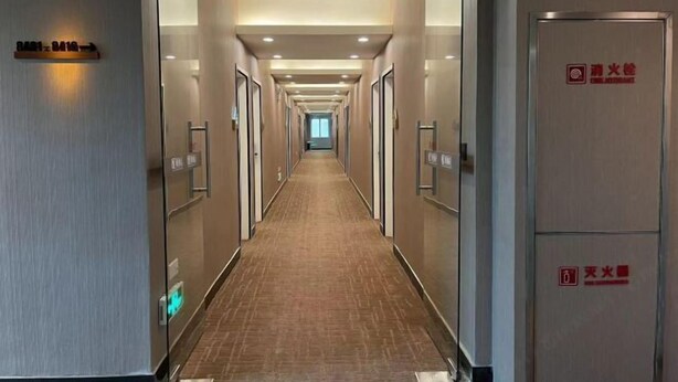 Pasillo de hotel con diseño alargado y estrecho, con puertas a ambos lados, piso alfombrado e iluminación empotrada en el techo.