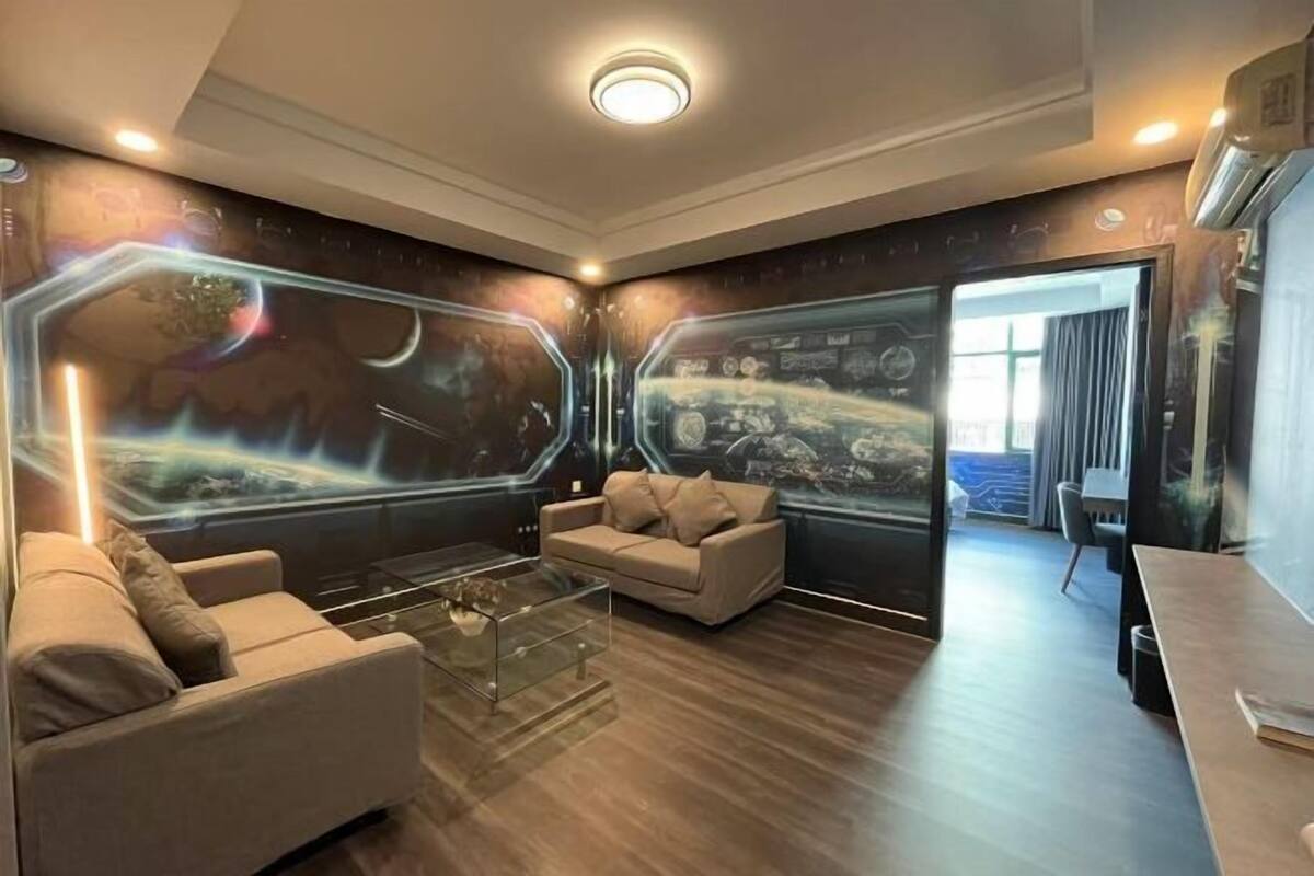 Un salon moderne avec un canapé, une table basse et un mur orné d’une fresque sur le thème de l’espace.