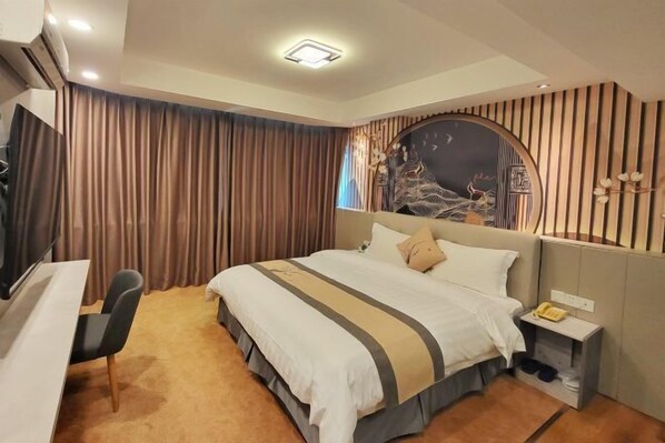 Habitación de hotel con cama, escritorio, silla, televisión y un cabecero decorativo.