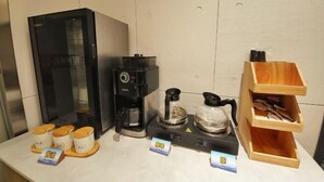 Una estación de café con cafetera, tetera y teteras, además de bolsitas de té y una caja de madera con bolsitas de té.