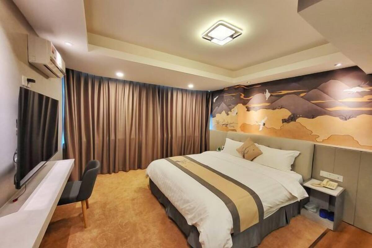 Une chambre d’hôtel avec un lit, un bureau, une chaise, une télévision et un rideau.