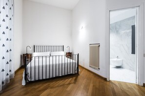 Une chambre à coucher comprenant un lit, des tables de chevet, un radiateur et une salle de bain avec un lavabo et un miroir.