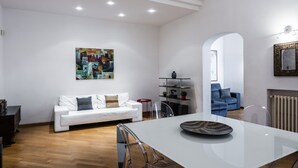 Ein modernes Wohnzimmer mit einem weißen Sofa, einem Esstisch mit Stühlen, einem Bild an der Wand und einem blauen Sessel im Hintergrund.