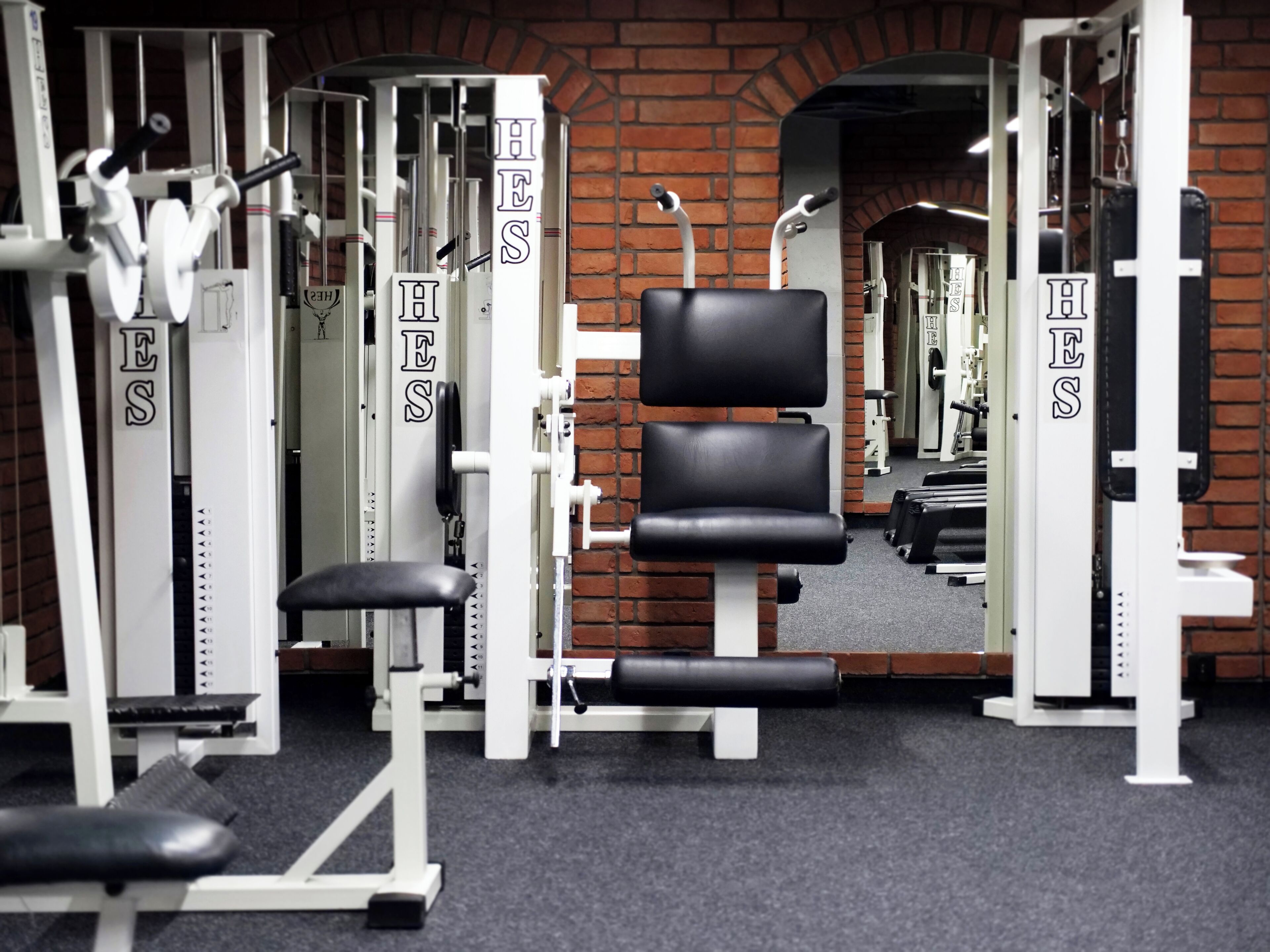 Un gimnasio con máquinas de pesas y una banca, con una pared de ladrillo y un espejo.