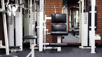 Un gimnasio con máquinas de pesas y una banca, con una pared de ladrillo y un espejo.