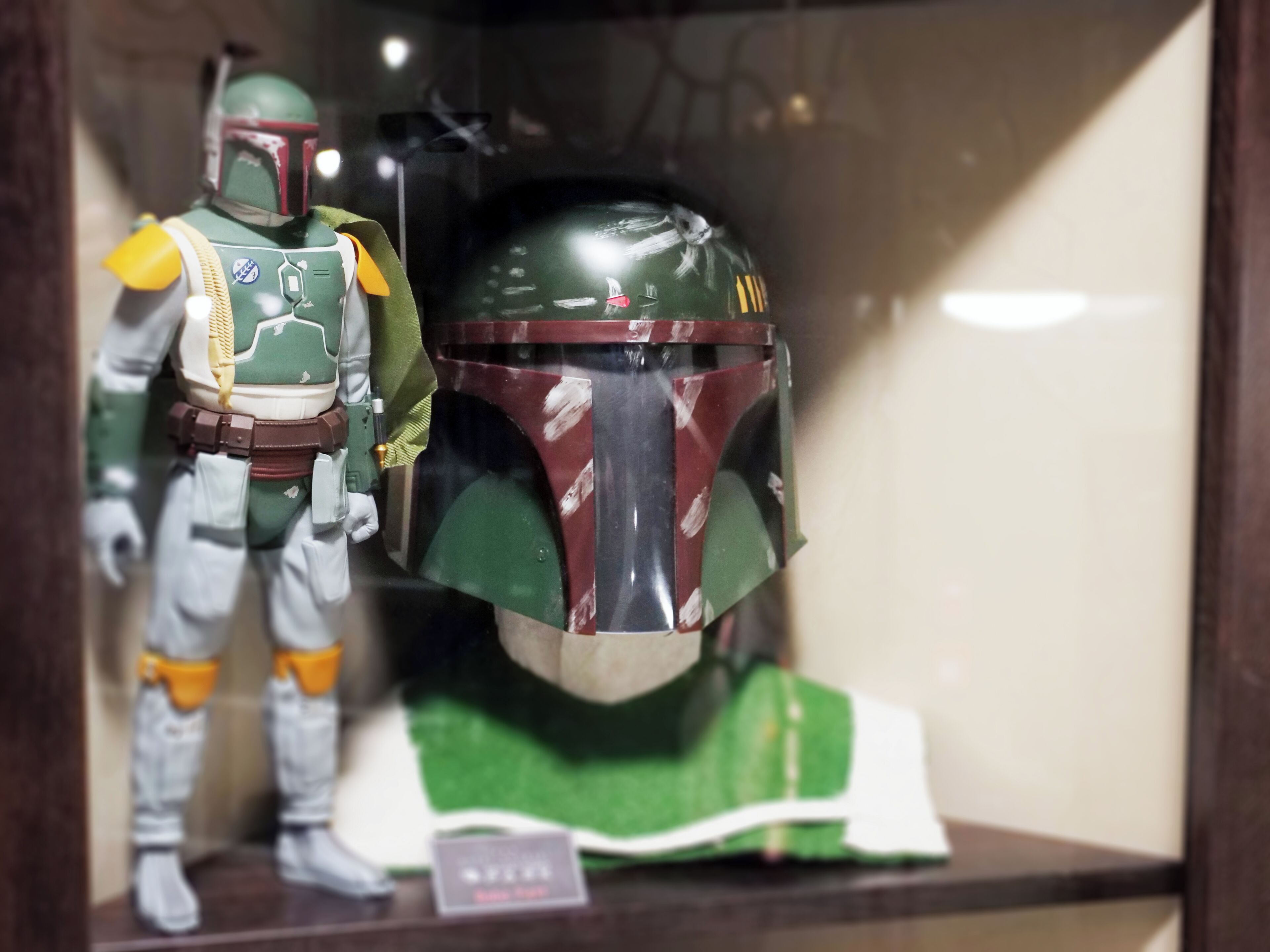 Una teca con una statuina di un personaggio in abito verde e bianco con elmetto, e un elmetto separato con motivo verde e rosso.