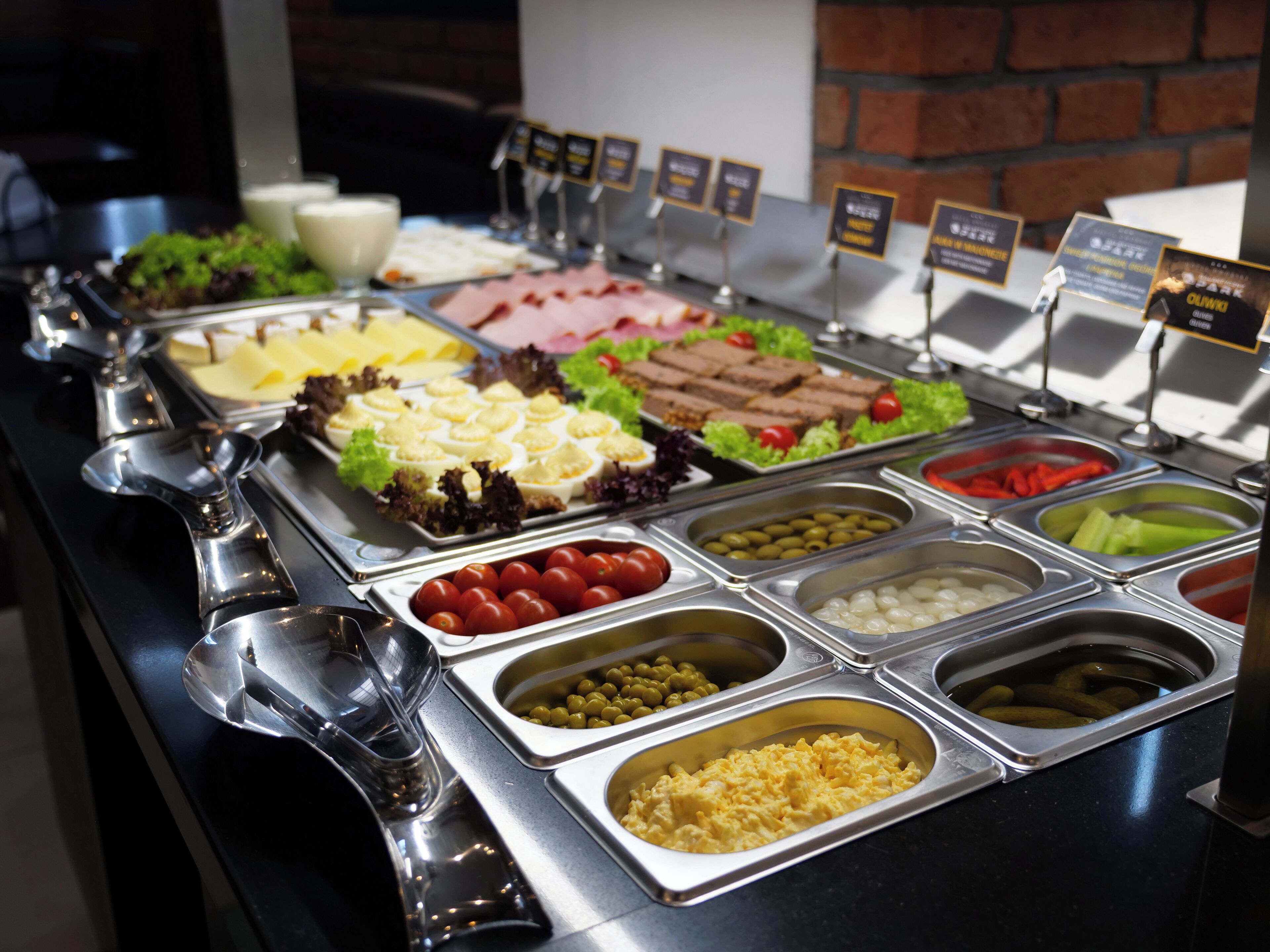 Buffet-pöydässä on tarjolla monipuolinen valikoima ruokia, kuten munia, lihatuotteita ja kasviksia.