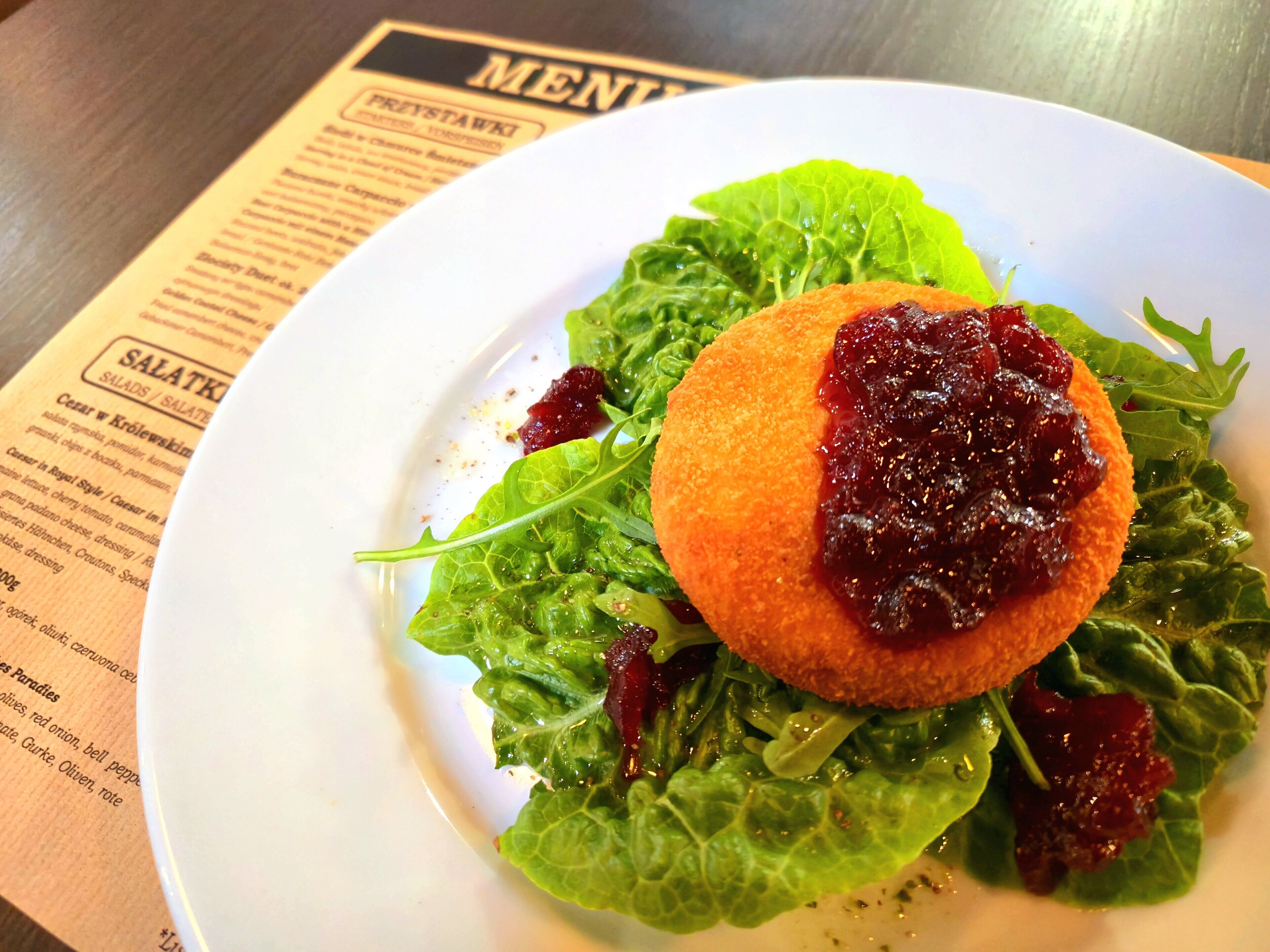 A plate with a salad and a breaded item on top, placed on a table with a menu in the background.