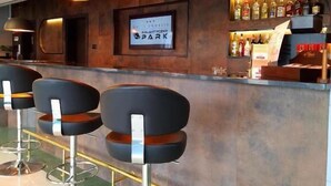 A bar area with modern stools, a counter with a sign, and a selection of bottles.