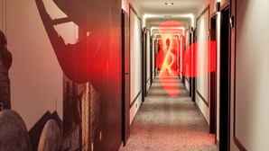 A hotel hallway with a carpeted floor, doors on both sides, and a wall with a large, abstract mural.