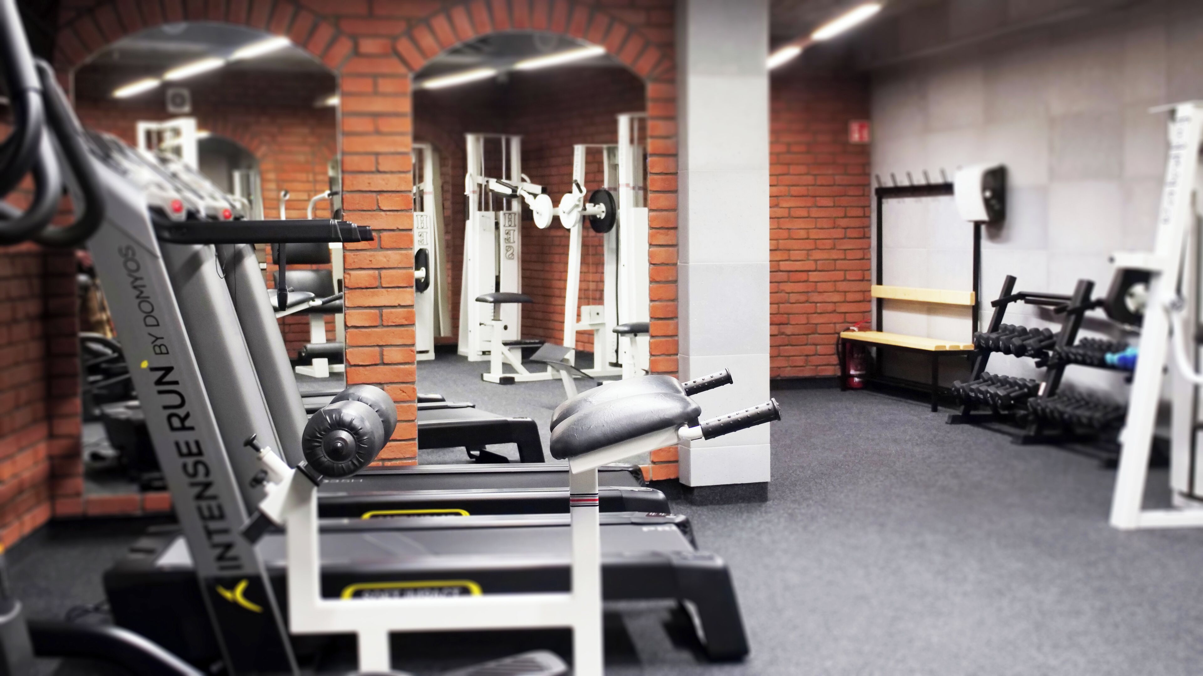 A gym with various exercise equipment, a brick wall, and a bench.