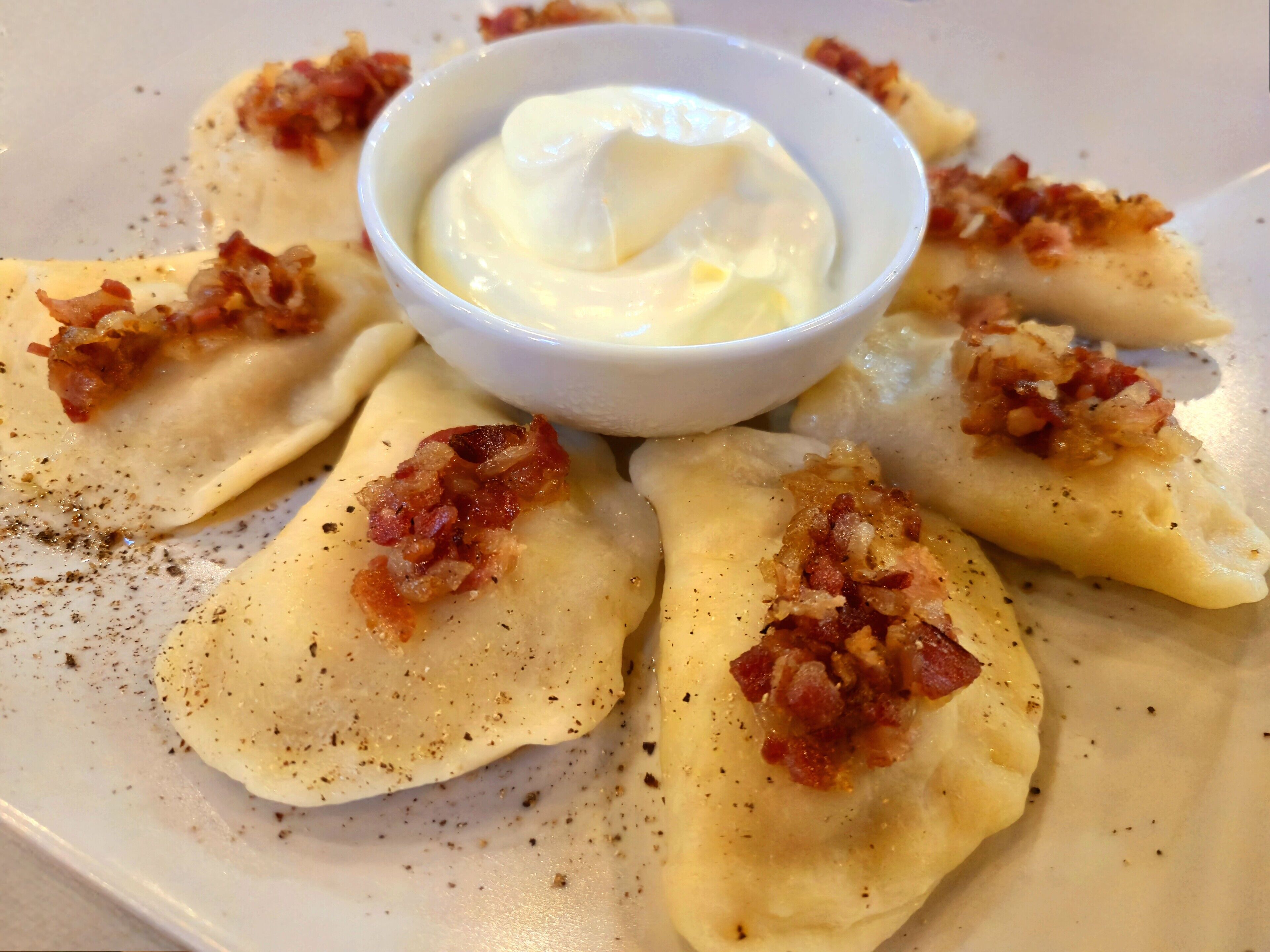 Un plato de pierogi acompañado de crema agria y trocitos de tocino.