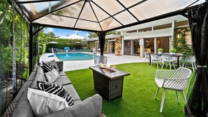 A covered outdoor area with a pool, a dining table with chairs, and a sofa with cushions. - 4BR Intracoastal Retreat With Pool, Games & More! (West Palm Beach)