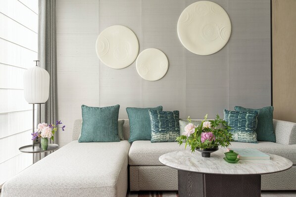 A modern living room with a sectional sofa, decorative wall art, a round coffee table, and a vase with flowers. - Four Seasons Hotel Hangzhou At Hangzhou Centre (Hangzhou)