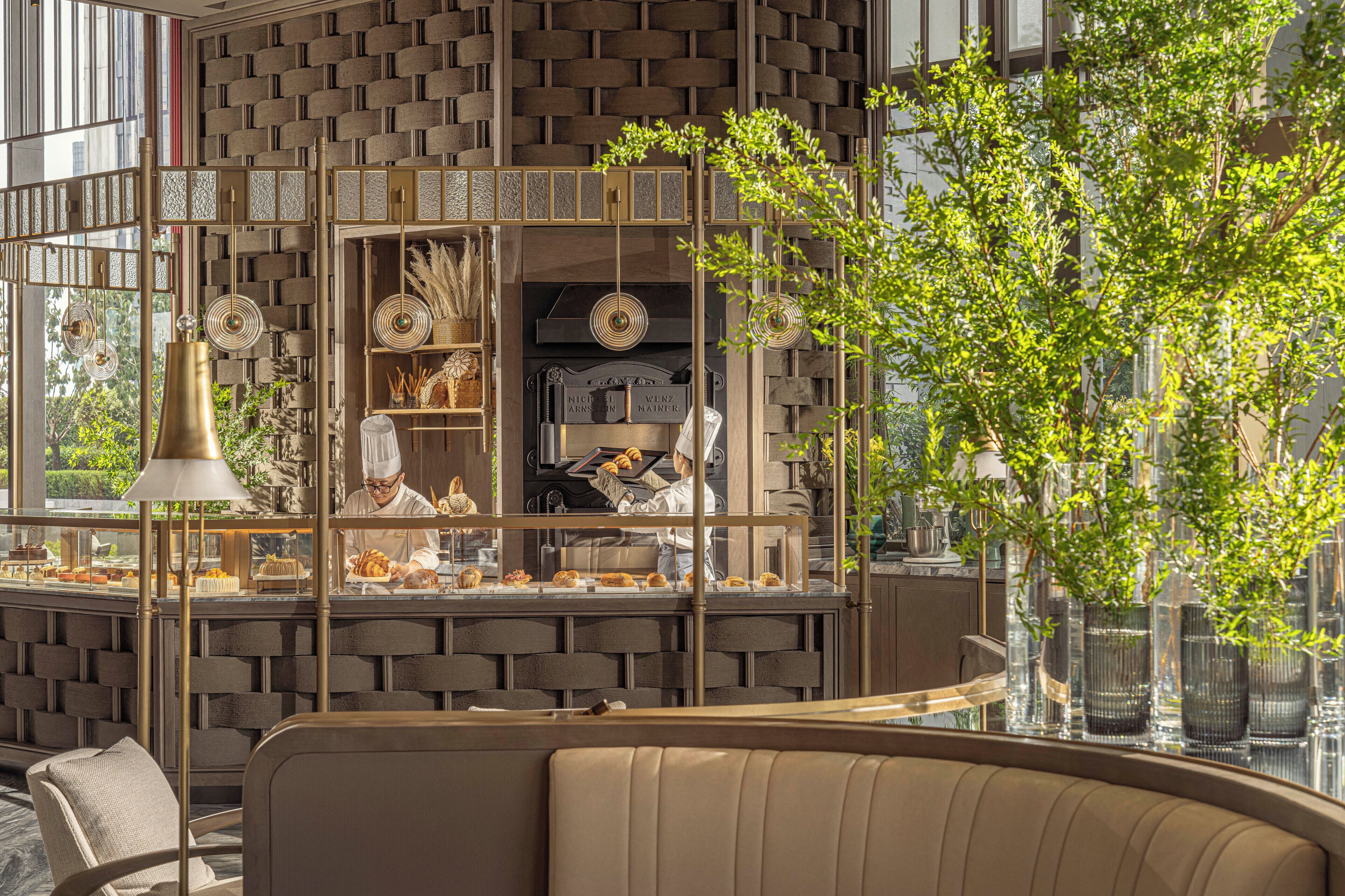 A modern interior with a brick-patterned wall, a glass display case with pastries, and a seating area with a cushioned bench.