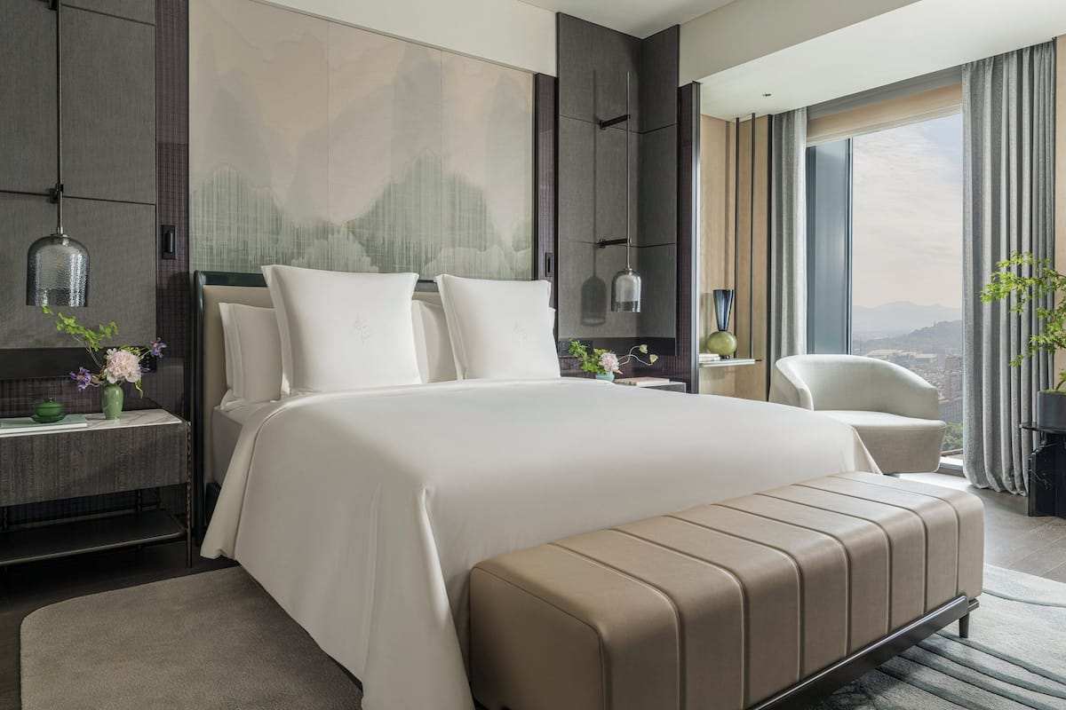 A modern hotel room with a large bed, a seating area, and a view of the city.