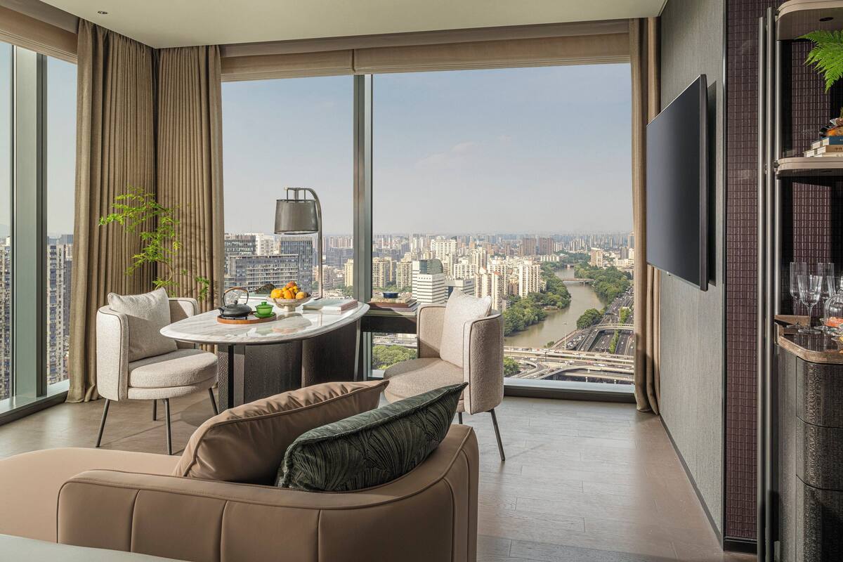 A modern living room with a city view, a dining area, and a TV mounted on the wall.