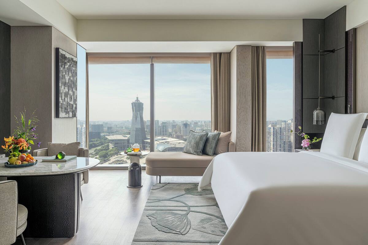 A modern hotel room with a large bed, a seating area, a dining table, and a city view.
