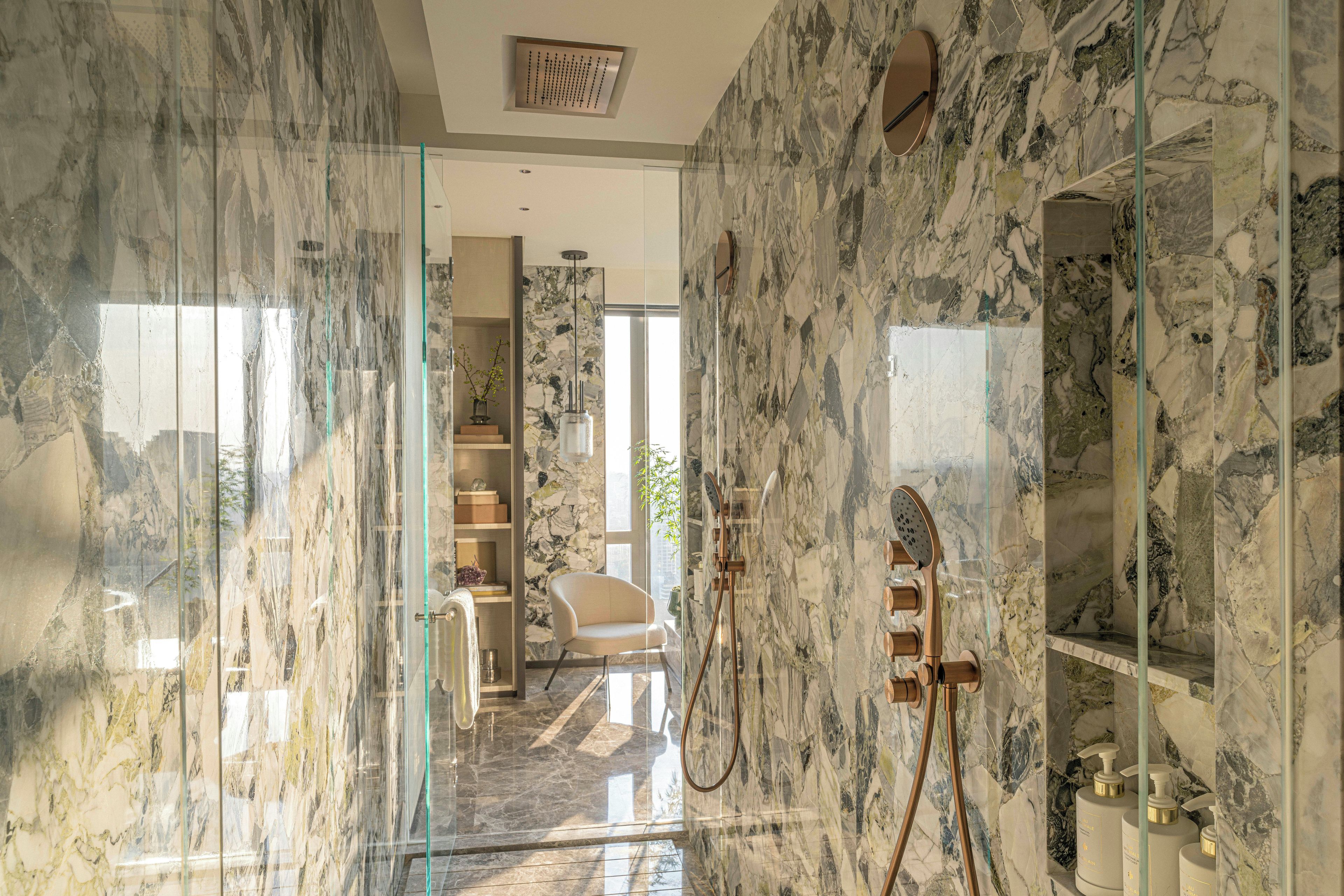 Un baño moderno con paredes de mármol, cabina de ducha con vidrio y ducha visible.