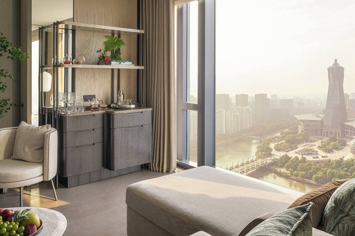 A modern hotel room with a city view, a dining area with a built-in kitchen, and a comfortable seating area.