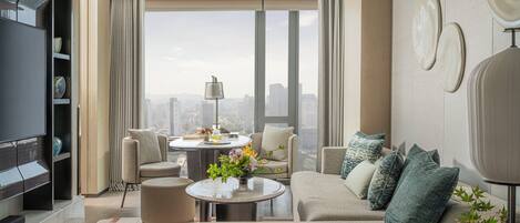 Una sala de estar moderna con sofá, mesa de centro y televisor, un comedor con mesa y sillas, y ventanas amplias con vista a la ciudad.