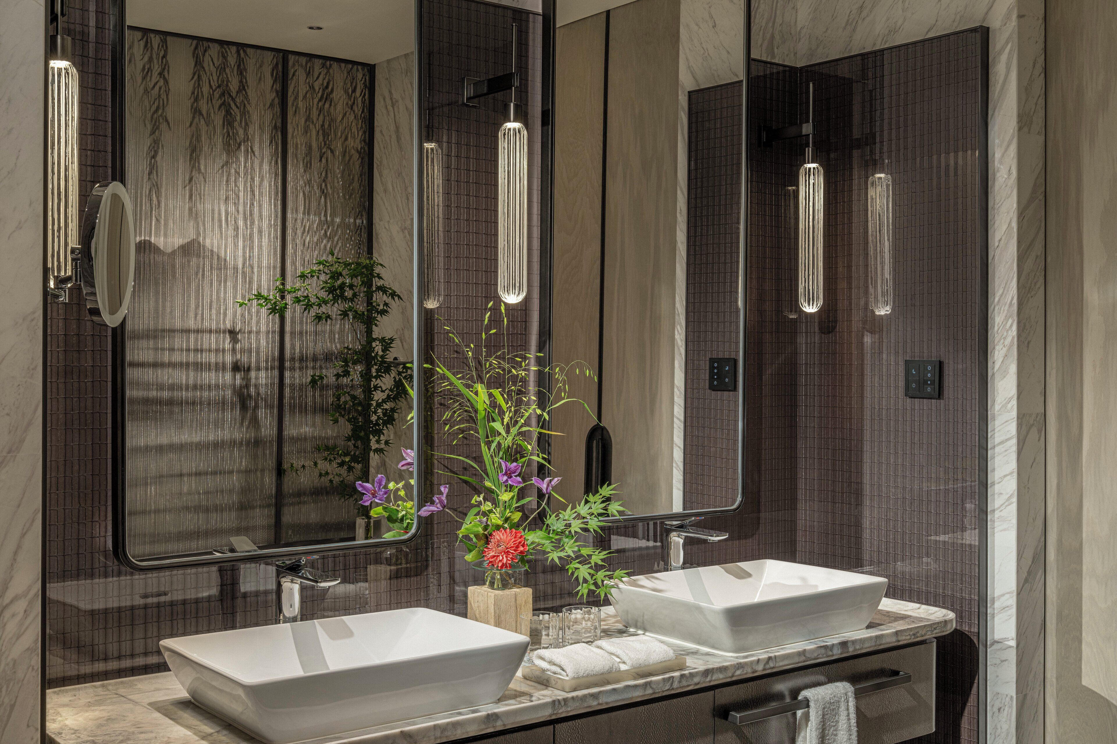 A modern bathroom with two sinks, a large mirror, and a hanging light fixture.