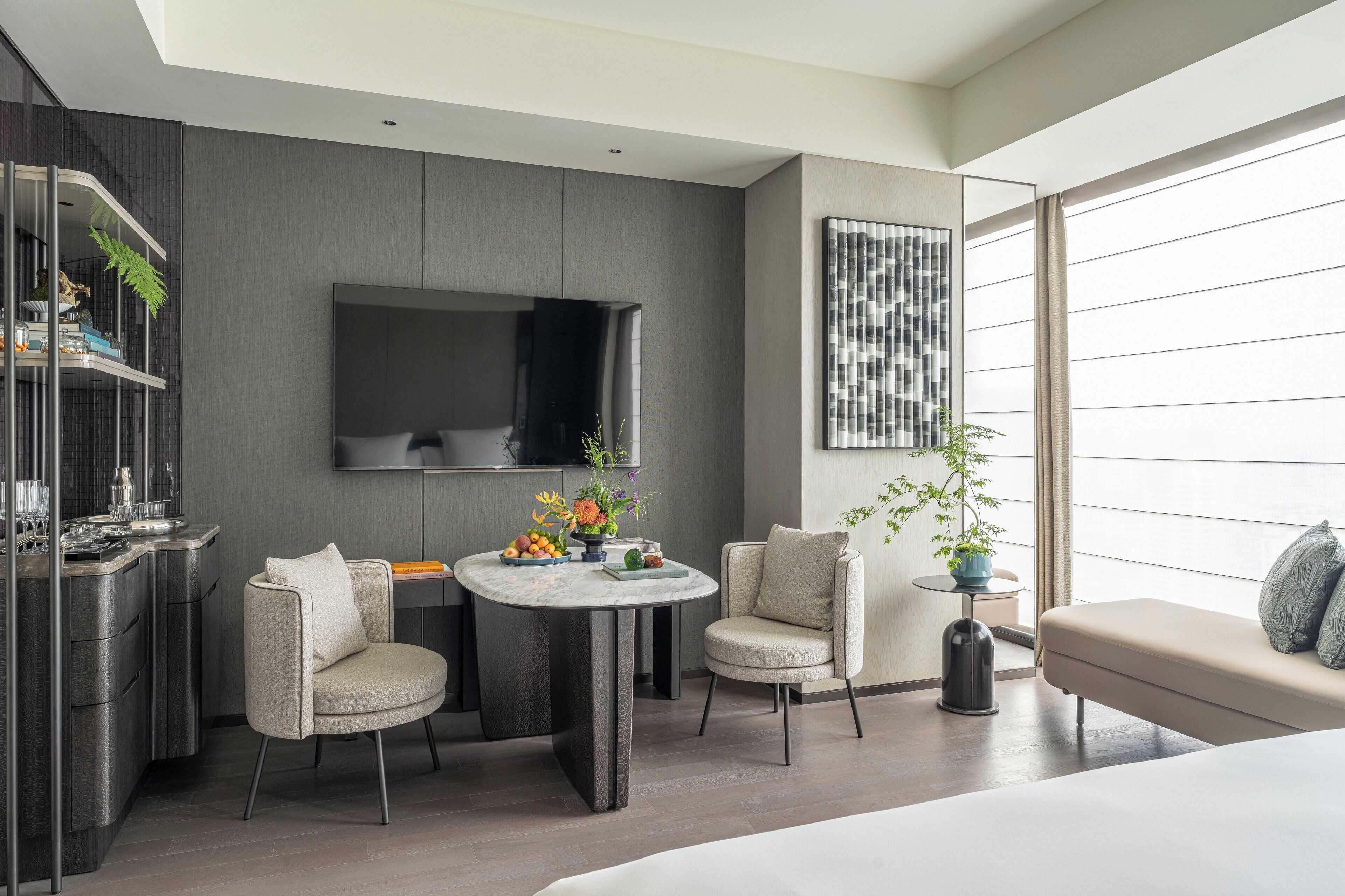 Una habitación de hotel moderna con zona de comedor, sofá y un amplio ventanal con cortinas.