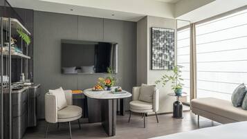 Una habitación de hotel moderna con zona de comedor, sofá y un amplio ventanal con cortinas.