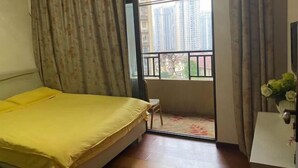 A bedroom with a bed, a small table, a window with a view of buildings, and a balcony. - Xiaowo Hostel (Chongqing)