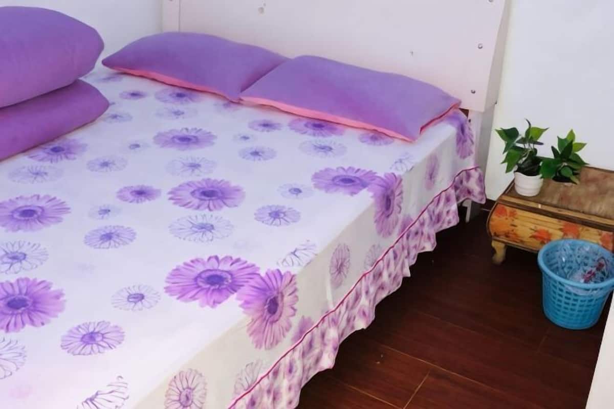 A bed with a floral bedspread, a small bedside table with a plant, and a blue laundry basket.