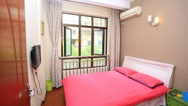 A bedroom with a bed, a window with curtains, an air conditioner, and a wall-mounted light fixture. - Xiaowo Hostel (Chongqing)