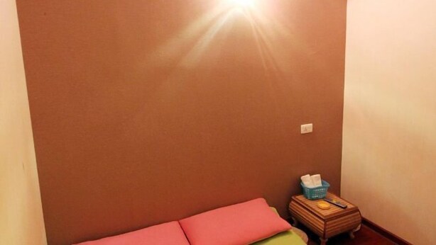 A small room with a pink bed, a wooden nightstand with a basket, and a wall-mounted light. - Xiaowo Hostel (Chongqing)