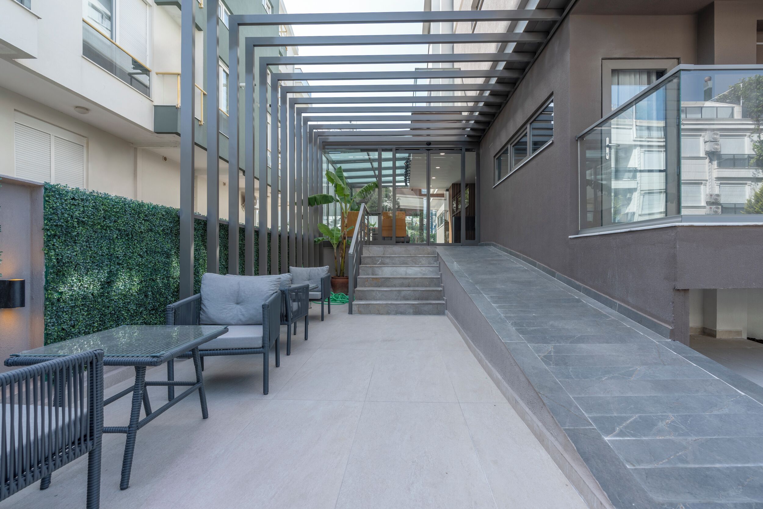A modern outdoor lounge area with a glass railing, outdoor seating, and a staircase leading to an upper level.