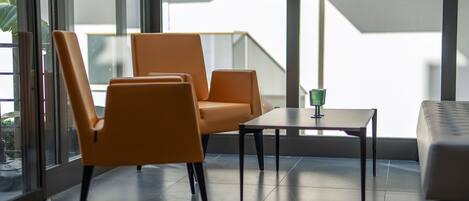 Una sala de estar moderna con dos sillas naranjas, una mesita y vistas a un edificio a través de amplias ventanas.