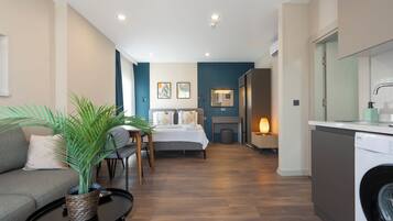 Quarto de hotel moderno com cama, sofá, mesa de jantar e máquina de lavar roupa.
