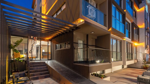 Een modern gebouw met een glazen balkon, terrasplekken en een trap naar de ingang.