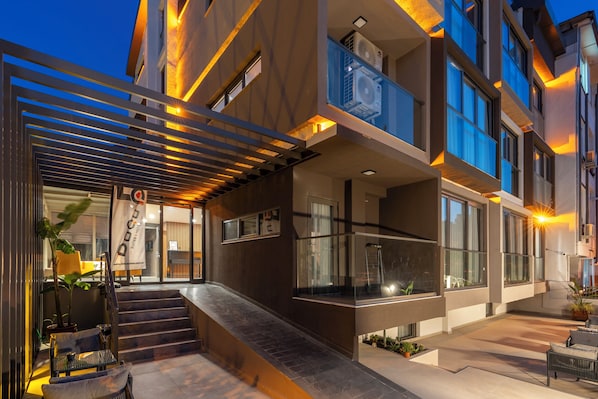 A modern building with a glass balcony, outdoor seating, and a staircase leading to the entrance. - Doqu Suites Hotel (Konyaalti)