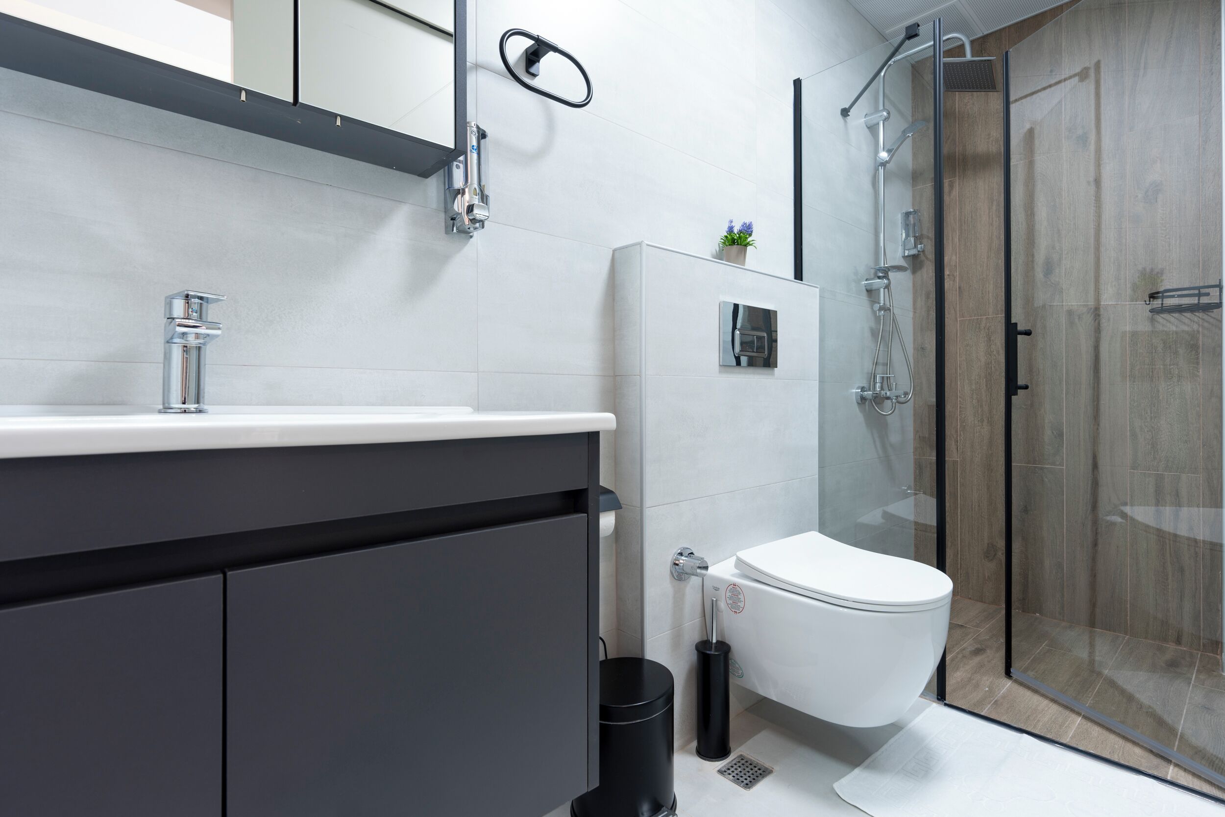 Une salle de bain moderne avec un lavabo blanc, des meubles sombres, des toilettes et une douche à parois de verre.