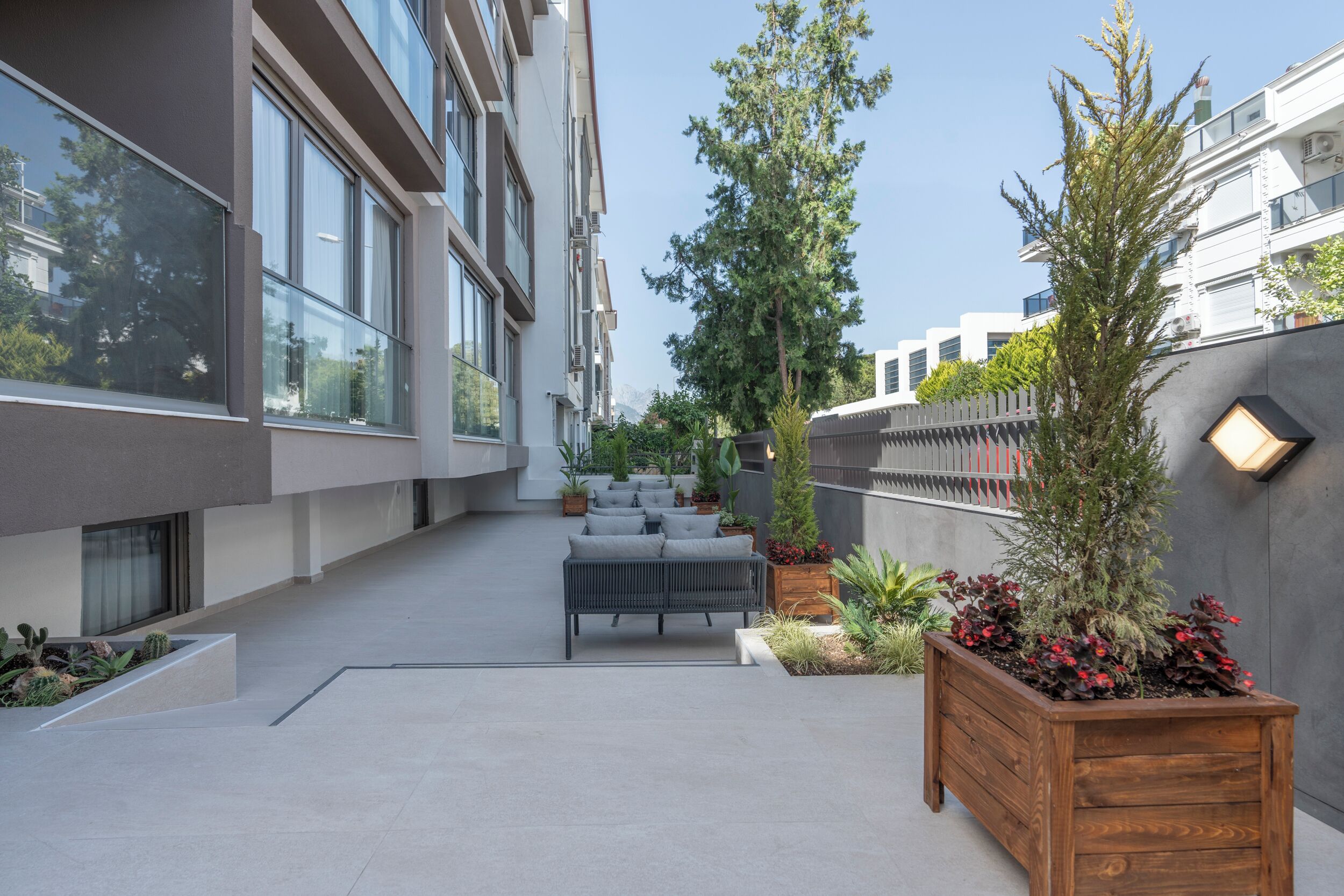 Eine moderne Terrassenausstattung mit einer Couch, Pflanzgefäßen und einer Holzbank.