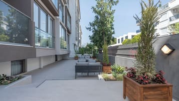 Un patio moderno al aire libre con un sofá, macetas y un banco de madera.